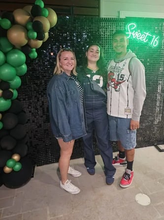 Ashlee and family in front of the black shimmer wall with sweet 16 neon sign in Logan.