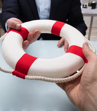 Photo of a male hand handing another man a lifesaver across desk. Insurance is a lifesaver..