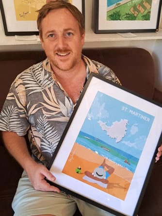 Artist smiling while holding a framed beach-themed print titled "Cloud Spotting"
