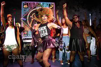 drag queen in "black lives matter" shirt dances toward audience surrounded by dancers.