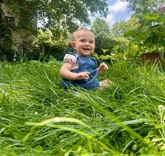 A happy baby girl sitting in the tall grace smiling at the camera representing mother baby bond