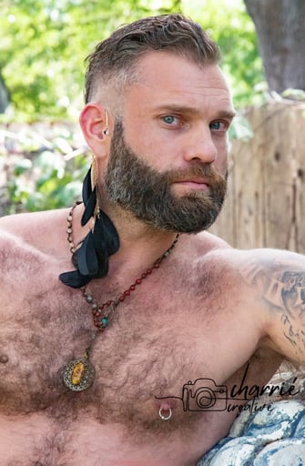 outdoor portrait of shirtless masseuse with a trimmed beard and hairy chest looking intrigued