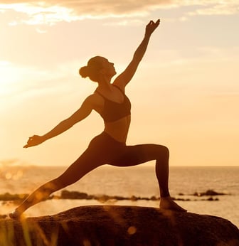 Uma mulher praticando yoga ao ar livre, em um cenário inspirador com o pôr do sol ao fundo. 