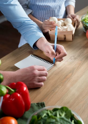 Man en vrouw werken samen aan een laptop en maken aantekeningen in een notitieboek.