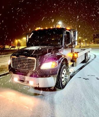 a tow truck with a flat bed in the snow at night with its lights on