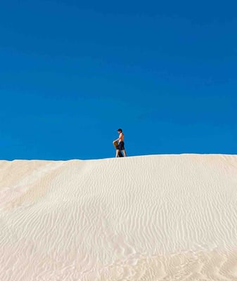 Man at the top of the sand dunes with his snowboard in Lancelin, Western Australia.