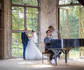 Ein Brautpaar küsst sich an einem Klavier in einer lichtdurchfluteten Umgebung.