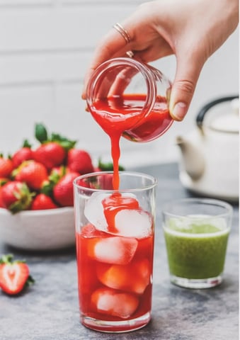 Pouring strawberry puree over ice in a tall glass.