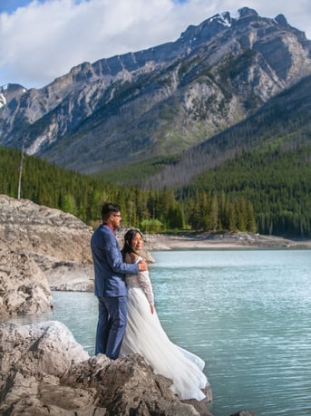 a bride and groom standing on a rock formation at lake minnewanka