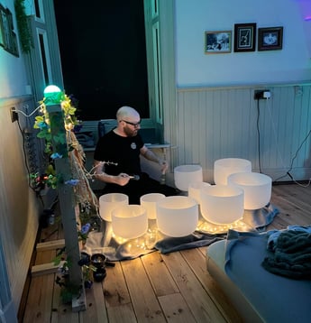 a man playing crystal bowls at night with fairy lights all around