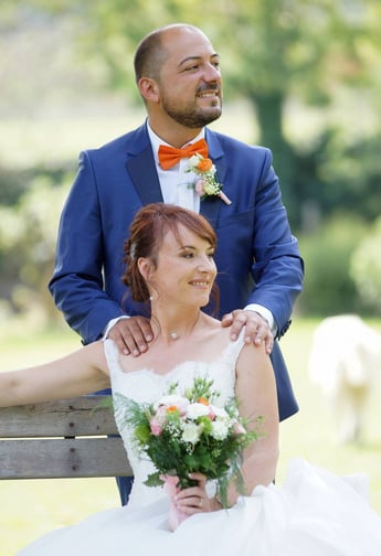 photo de couple pendant un mariage. la mariée est assise avec son bouquet comportant du orange