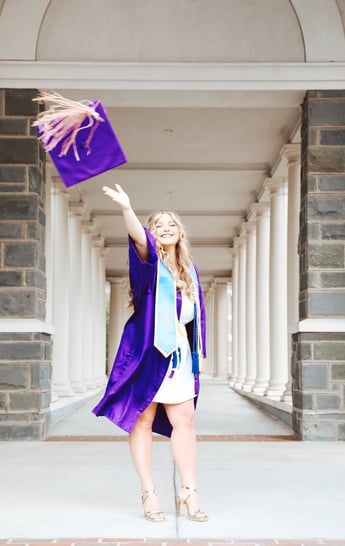 A woman in a purple graduation gown throwing a purple graduation cap
