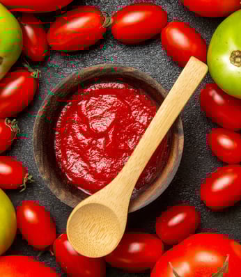a bowl of tomato sauce with tomatoes and a wooden spoon