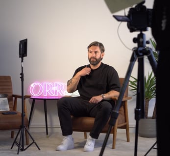 a man sitting in a chair with a pink neon sign