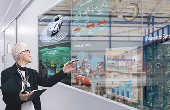 a woman in a black jacket and glasses is pointing at a transparent display of cars