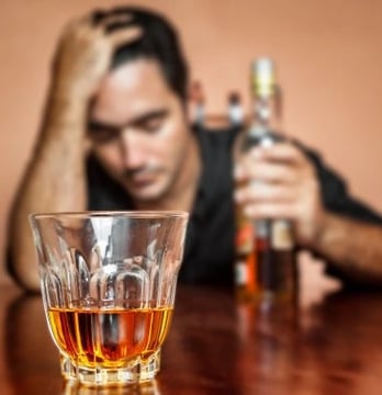 homme 1 bouteille d'alcool à la main gauche main droite sur la tête et verre devant lui presque vide