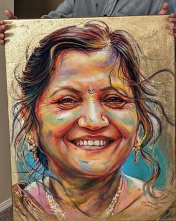 Artist S.K. Gusani holding a memorial painting of a smiling woman, gold leaf, portrait art