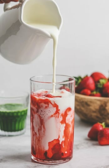 Milk being poured over strawberry layer in iced glass