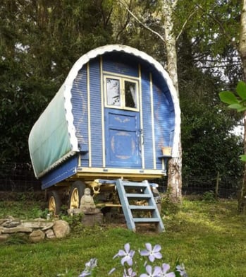 Colorful bow-top gypsy wagon with blue and yellow paint, garden roulotte with ladder entrance, Buddh