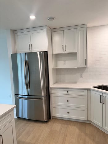 Corner view of a modern kitchen with white shaker cabinets, deep drawers, quartz countertops, and a 