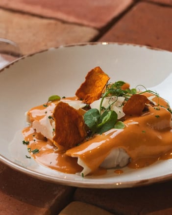 Canelón de temporada con salsa de sobrasada y crujientes, acompañado de una copa de vino tinto en ambiente rústico.