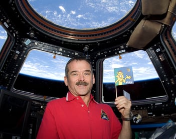 L'astronaute Chris Hatfield, en chemise rouge, tient un drapeau à bord de la Station spatiale