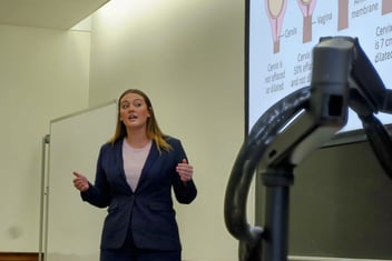 A woman with long hair in a blue suit presenting a pitch
