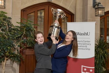 Two women in suits lift a trophy above their heads