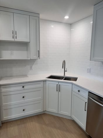 Corner sink area with white shaker kitchen cabinets, quartz countertop, subway tile backsplash, and 