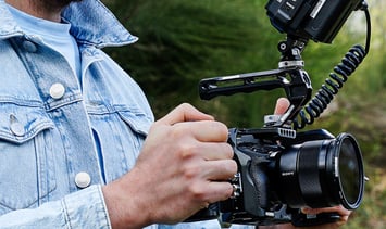 Mann in blauer Jeansjacke, draußen, mit Kamera Rig in den Händen, von der Seite