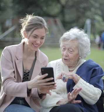 Young woman and elderly woman using smartphone together on a bench