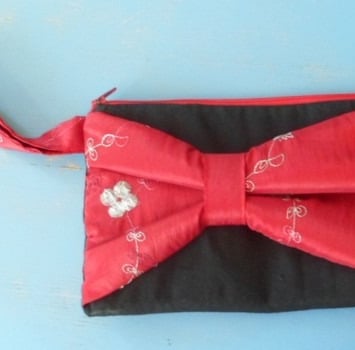 Pochette noire avec un gros nœud rouge en soie brodé de petites fleurs crème en fil de soie 
