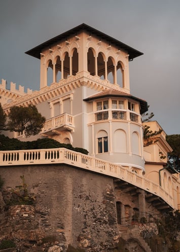 Elegant, cream-colored historical villa with ornate arches perched on a rocky cliff in Bogliasco