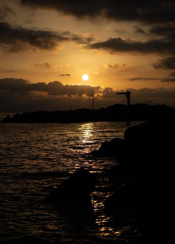 Silhouette of a rocky - shoreline shimmering reflection of the setting sun on the water - Bogliasco