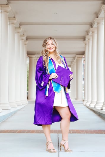 A woman in a purple graduation gown holding a purple graduation cap