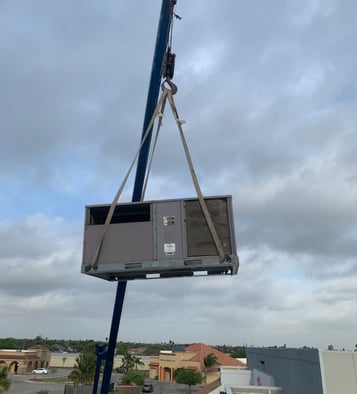 a crane is lifting a ac unit to replace and install