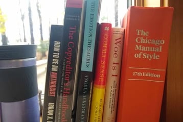 A coffee cup on a windowsill next to a bunch of writing and editing resource books