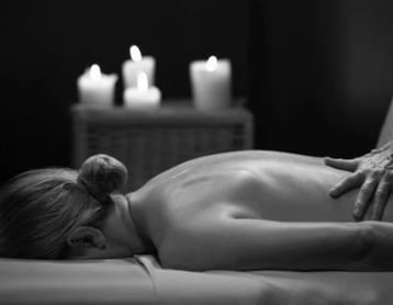 Woman lying on her front enjoying a massage, there are candles glowing in the background