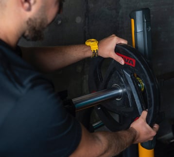 Antrenor montând o greutate pe bara de antrenament, ilustrând atenția la detalii