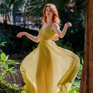 Ragazza in mezzo alla vegetazione con un abito dorato svolazzante