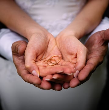 marito e moglie con le mani a cucchiaio che sorreggono le fedi
