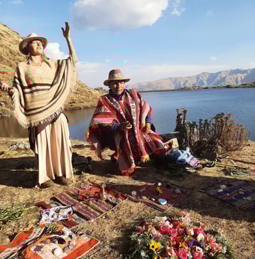 a woman in a traditional dress and a man in a hat opening sacred space at a mountain lake