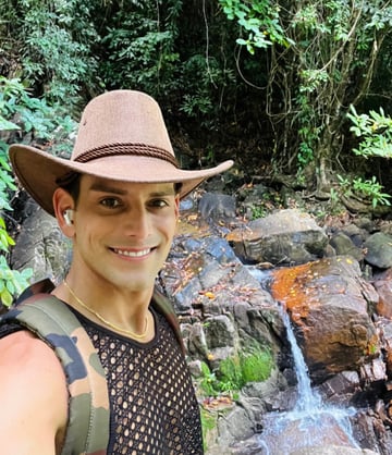 Travel writer Rick Silvia smiles at the camera wearing a cowboy hat in front of a waterfall