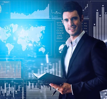 Business leader holds a notebook, while standing in front of a wall-sized screen displaying various charts and diagrams.