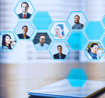 A tablet rests on a desk as holographic honeycomb shapes with headshots of businesspeople emerge from the screen.