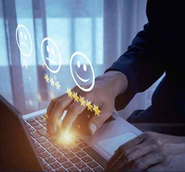 A leader types on a laptop as holographic sad, neutral, and happy faces appear to measure customer satisfaction, face unseen.