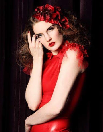 a woman in a red dress poses with a red flower in her brown curly hair