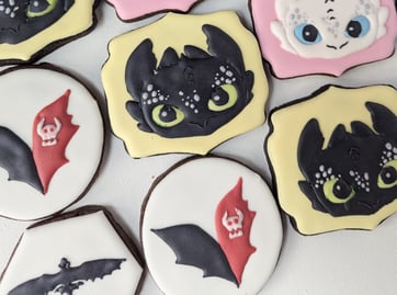 Cookies with yellow or pink icing, designed with How to Train Your Dragon characters