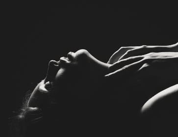 Woman lying down with her hands up by her neck.