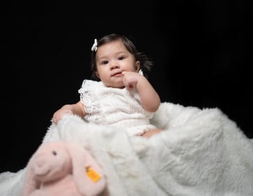 a baby girl sitting on a blanket with a pink stuffed animal